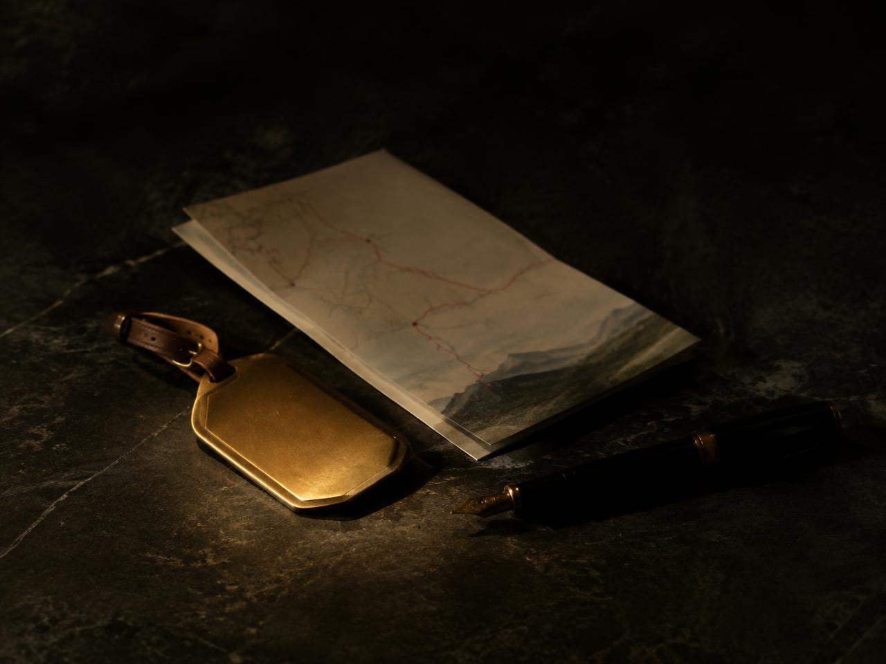 Brass luggage tag, folded map and fountain pen on dark stone